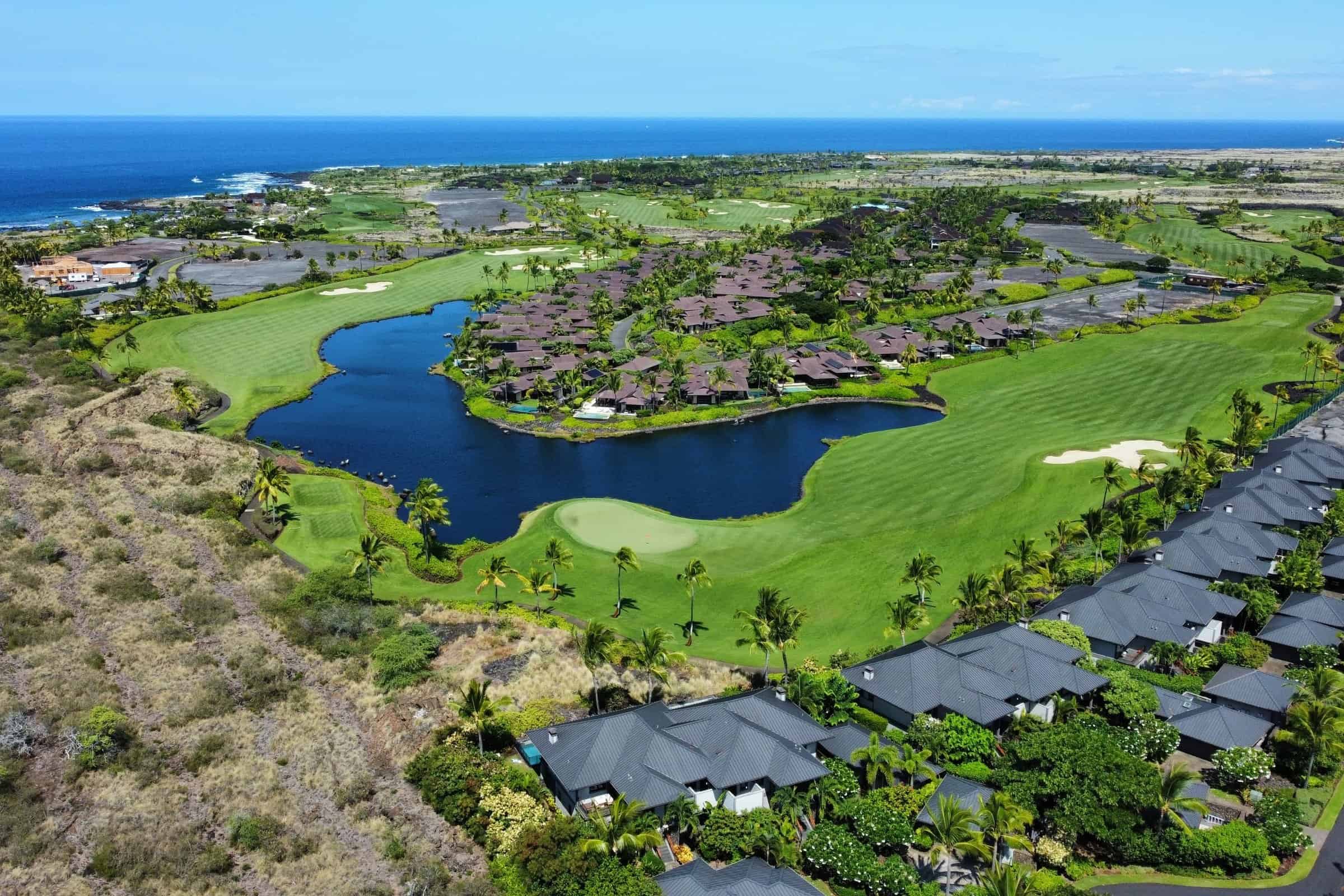 Aerial of the Kohanaiki golf course with a lake, greens and homes along the fairways.