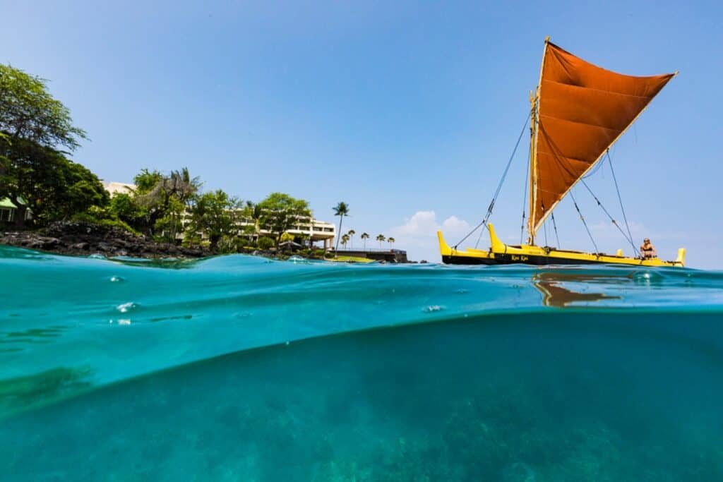Beautiful Big Island Hawaii sailboat with vibrant orange sail near Kona coast.