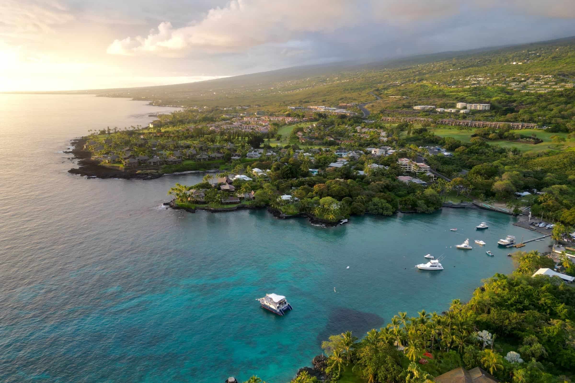 Aerial of Keauhou Bay with moored boats and homes along the Kona coastline.