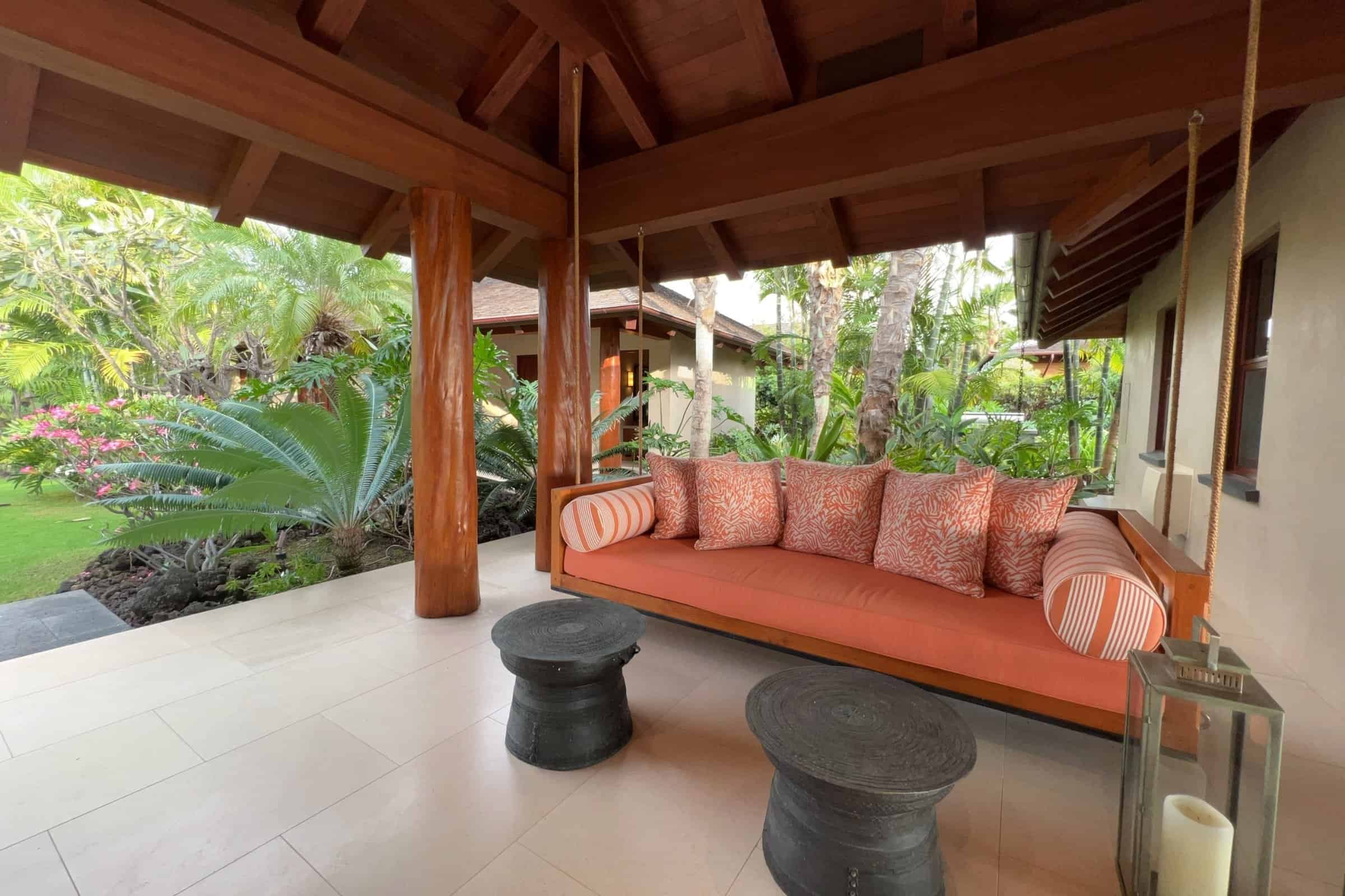 Covered lanai with a built-in daybed and coral cushions opening to the garden at a Kohanaiki home.