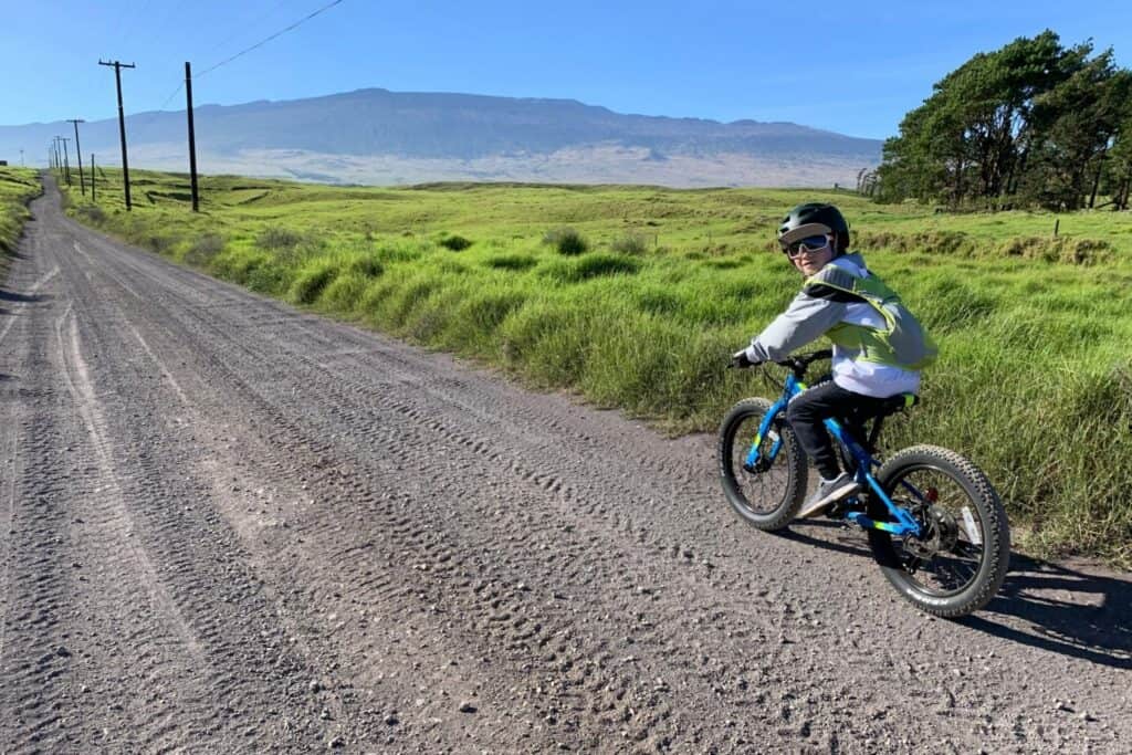 Child riding a bike on a dirt road in rural Big Island Hawaii with lush greenery and distant mountai.