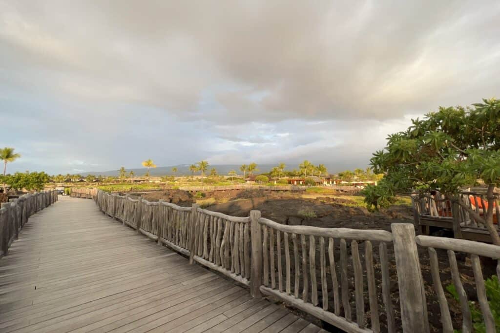 Boardwalk with a timber rail crossing lava terrain toward the mountains at Kohanaiki.