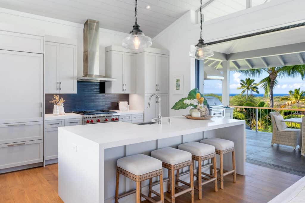 White contemporary kitchen with an island and stools opening to an ocean view.