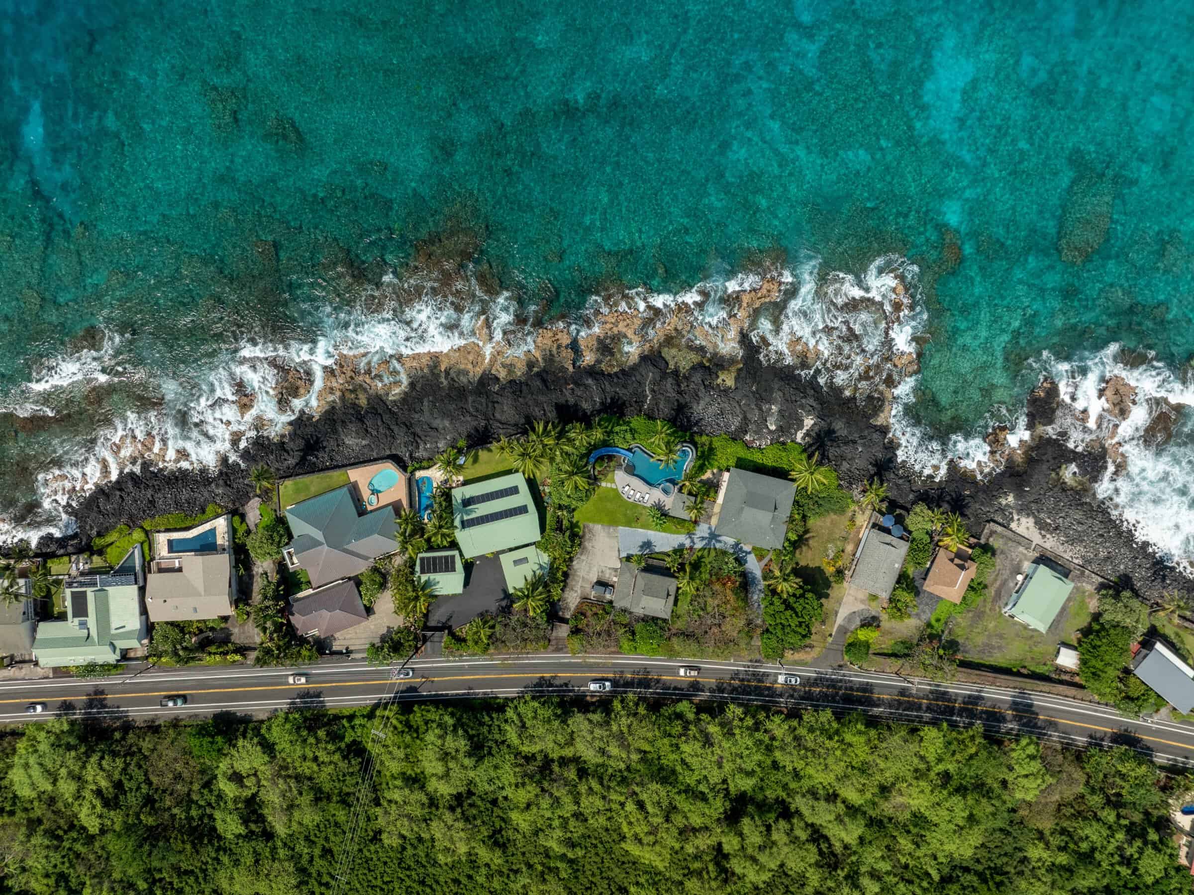 Aerial straight down over oceanfront homes and surf along the North Kona lava shoreline.
