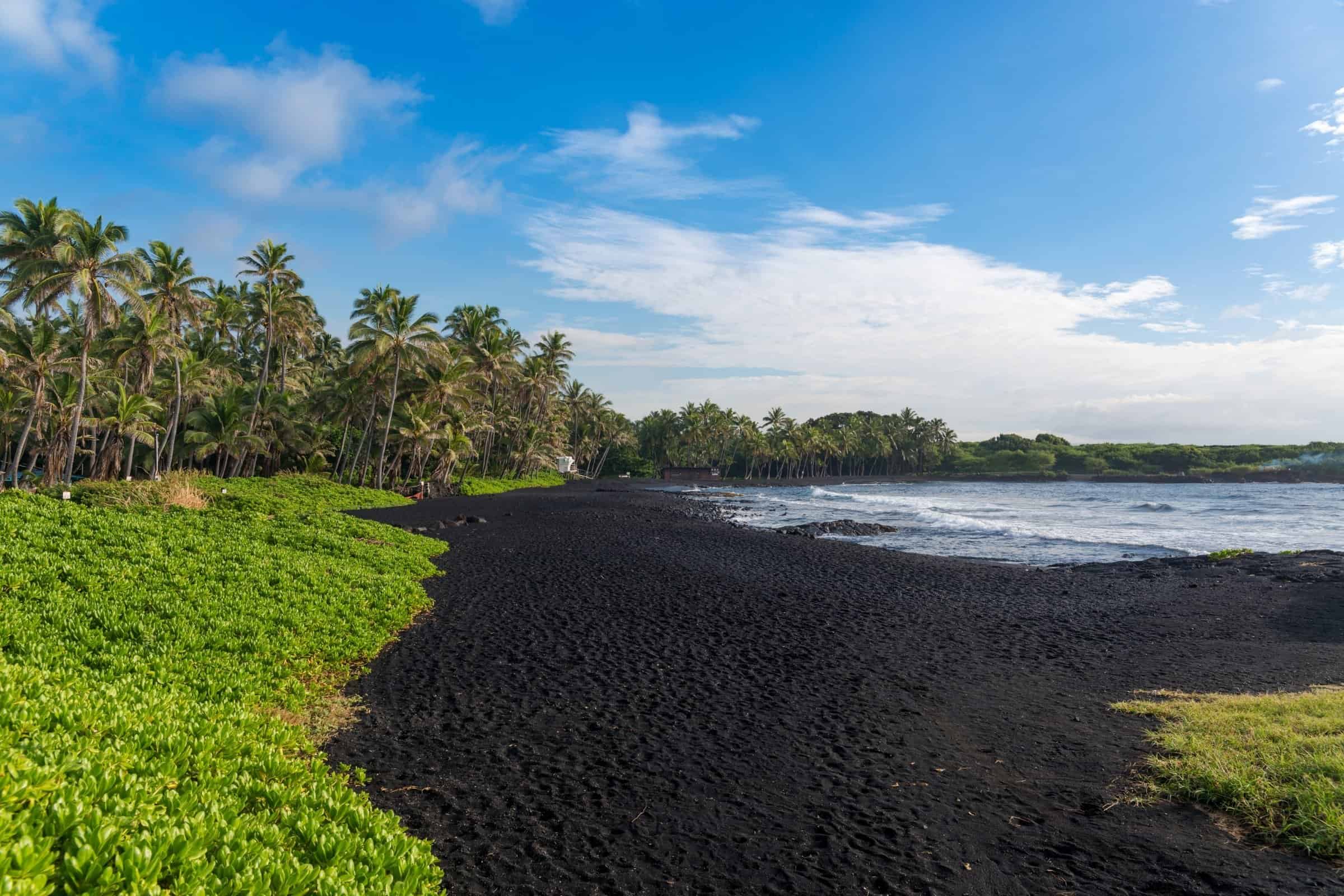Oceanfront land in Kona with lush tropical foliage and black sand beach.