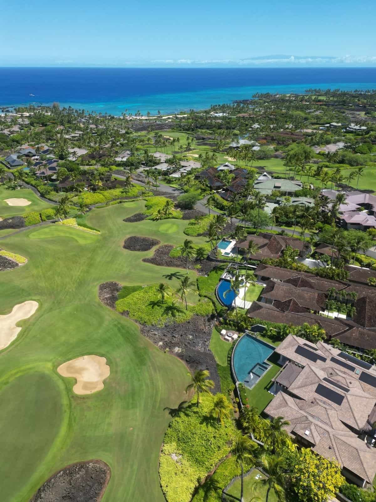Aerial of the Kukio golf course with homes and pools along the fairways.