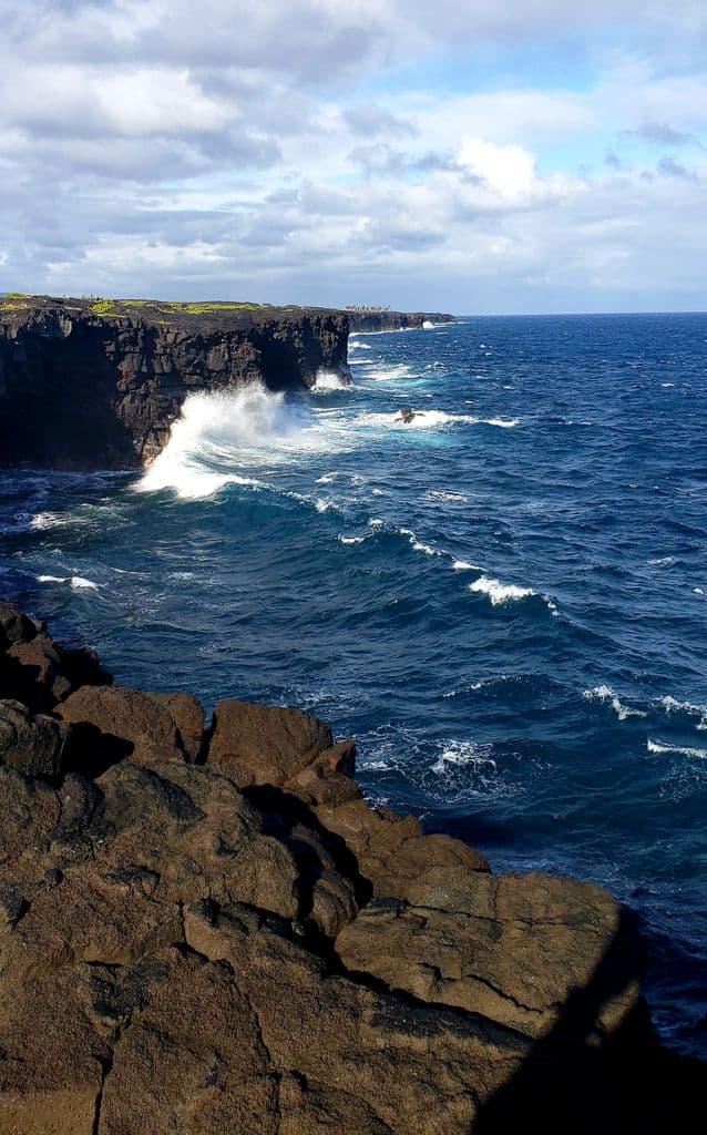 Dramatic ocean cliffs with waves crashing against the rock formations under a bright sky.