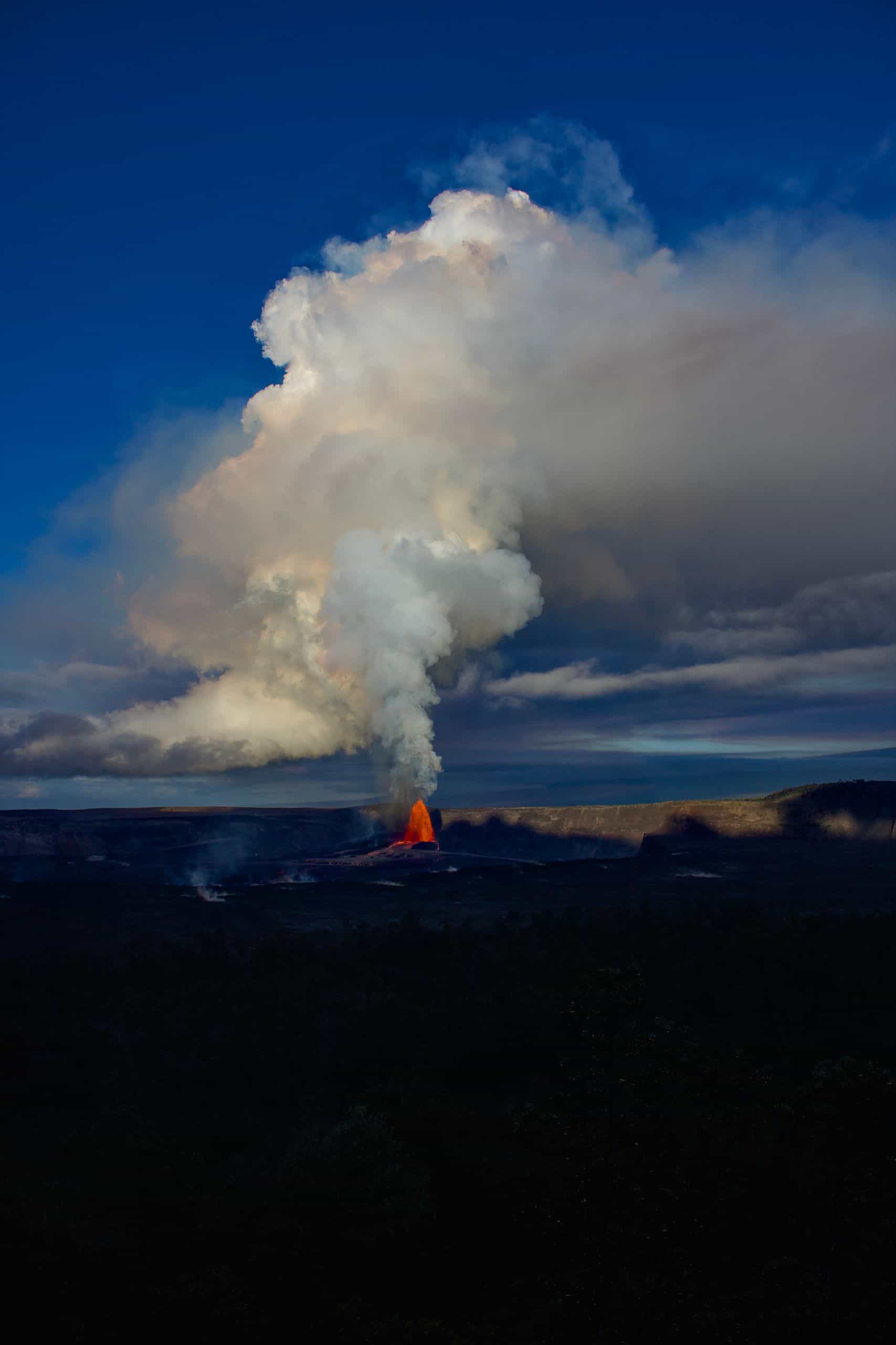 Active volcano on Big Island Hawaii with lava and smoke, scenic landscape, and dramatic sky.