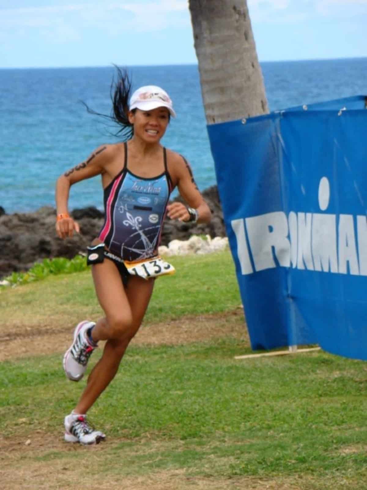 Rani Henderson running past an IRONMAN™ banner over the lava rock in Kailua-Kona.